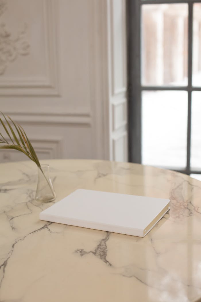 White mock up notepad placed on round table with green branch of plant in modern light room with window at home